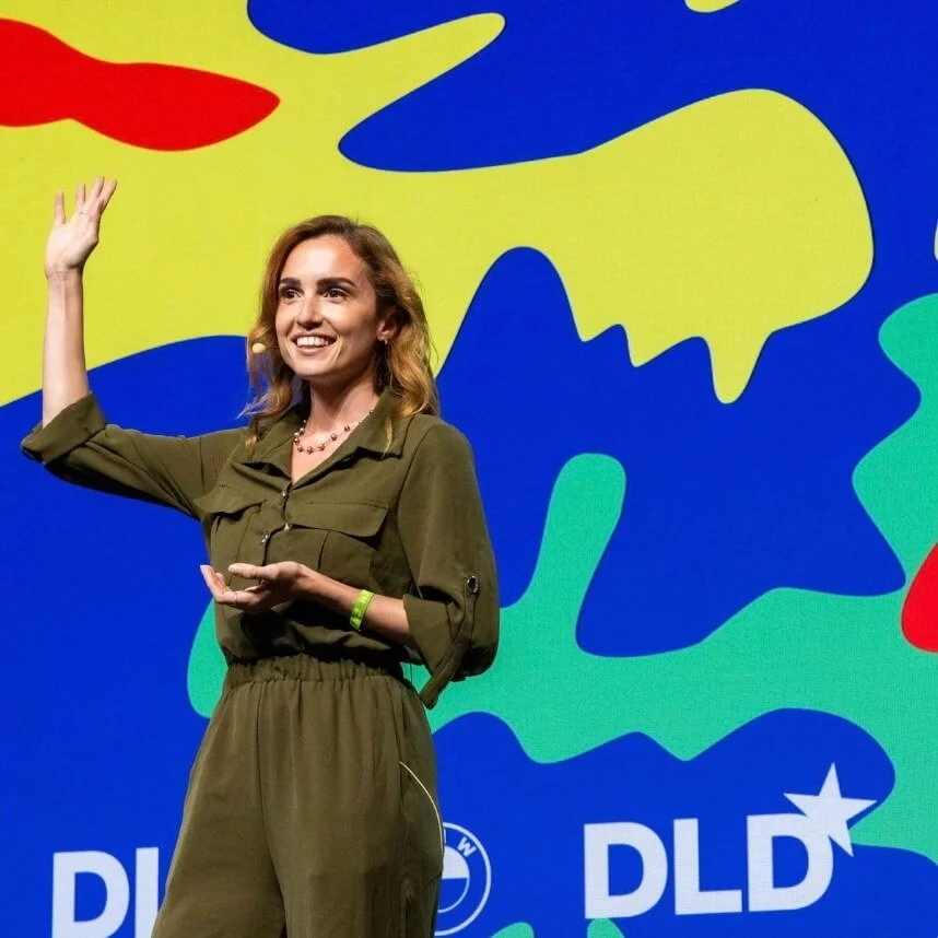 Alessa Berg on stage at DLD, waving, against a colourful backdrop